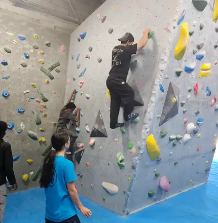 A climbing wall with two Handcrafted residents on it. Stood on the floor below is a Handcrafted housing support worker, who look