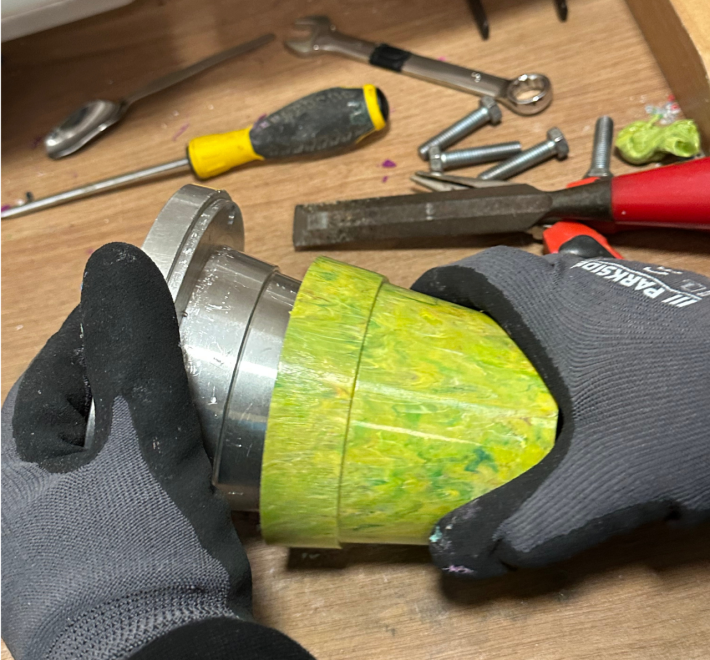 An in-action shot of the plant pot being made. A trainee is taking the yellow plant pot off the metal mould.