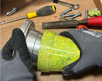 An in-action shot of the plant pot being made. A trainee is taking the yellow plant pot off the metal mould.